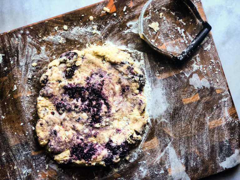 Raw scone dough, swirled with blackberries sits on a cutting board covered in flour
